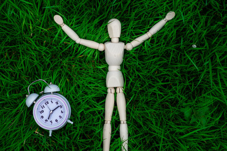 Time for holidays, rest, relaxation. The figure of a man and an alarm clock on the green grass. The...