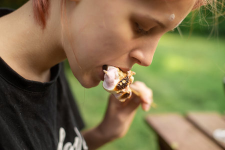 Girl eating marshmallow fried on the grill. close-up. Sweet snack on the go.
