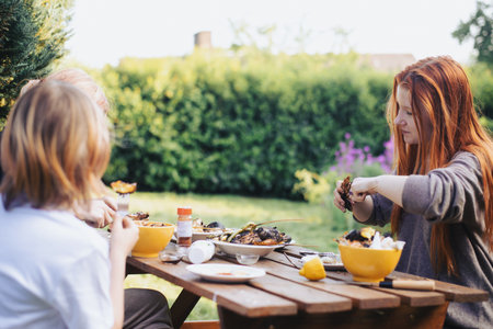 Lunch in the courtyard of the house on a wooden table. A young girl and children are eating.の写真素材