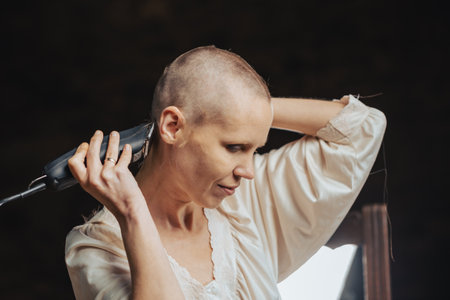 Portrait of a bald woman cutting her hair with a clipper on a dark background.の写真素材