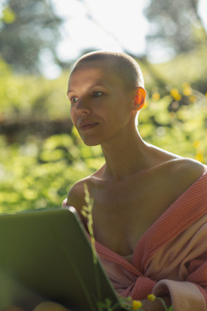 Thoughtful woman with laptop in nature. Sunny day, summer time. Work remotely, freelance, online shopping.の写真素材