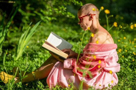Woman and reading a book outdoors. A bald woman in a bathrobe holds a book in her hands, sits on the green grass. rest, recovery.の写真素材