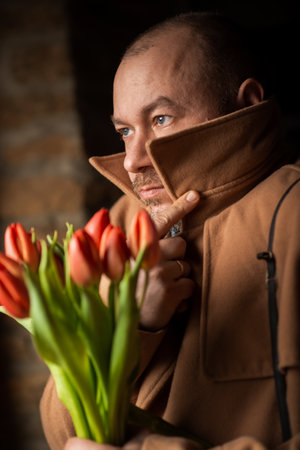 A man with a bouquet looks away in a dark room. Waiting for a meeting, a date.の写真素材