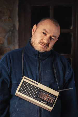 A middle-aged man with a retro radio looks at the camera. dark background.