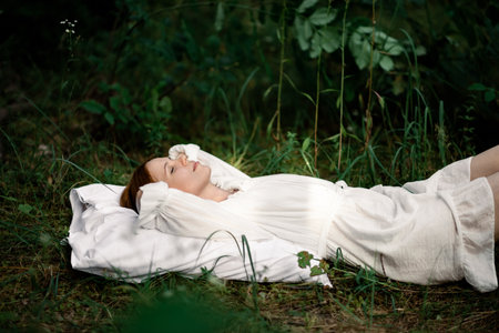Healthy sound sleep. Rest, relaxation in the forest. Woman sleeps on a pillow on a green glade in the forest.の写真素材
