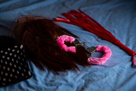 Handcuffs with red fur, whip and wig. Devices for love games on the bed.の写真素材