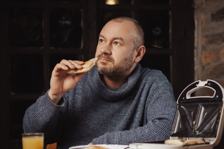 The man is having breakfast. An ordinary middle-aged man in a sweater is preparing to eat a sandwich...