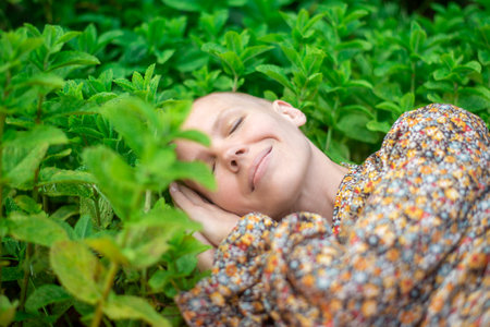 Woman sleeping in green mint leaves. Healthy sleep, aromatherapy concept. Adjusting the circadian rhythm. A bald woman smiles in her sleep.の写真素材