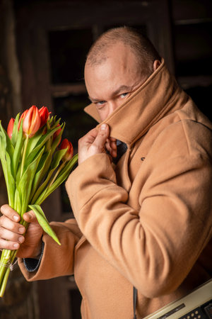The man with the bouquet covered his face with the hem of his coat. Anonymous meeting, incognito. Waiting for a meeting, a date.の写真素材