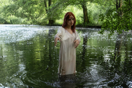 A young teenage girl in a white dress stands in a lake against a background of green foliage. day Ivan bathed.の写真素材