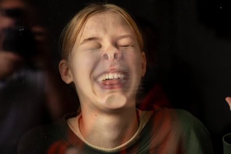 Portrait of a teenage girl through her face pressed against the glass on a dark background. Funny anticsの写真素材
