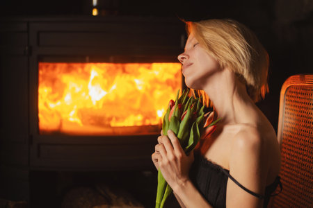 Middle-aged woman with a bouquet of tulips against the backdrop of a burning fireplaceの写真素材