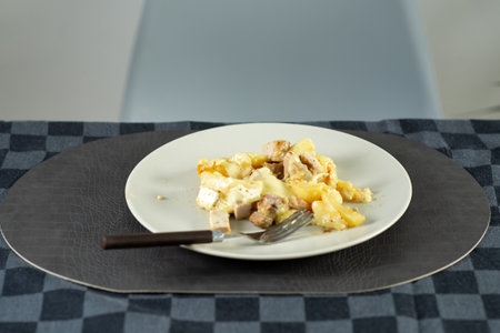 Fried stewed potatoes with meat and Brie cheese on a plate at the dinner tableの写真素材
