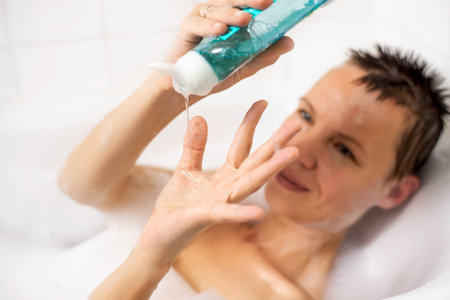 A woman takes a bath with foam. She pours gel onto her palm in the showerの写真素材