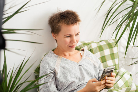 A middle-aged woman spends her entire day in bed, staring at her phone. Emotional decay, laziness, doing nothing.の写真素材