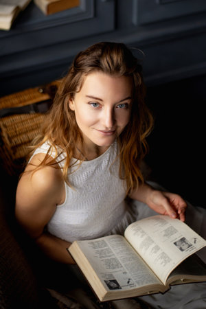 With an aura of elegance, a young lady smiles while engrossed in a book, her long hair cascading, seated comfortably on the sofa. It epitomizes the delight of reading and a deep affection for literatureの写真素材