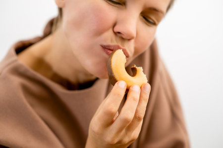 Decadent delight: An attractive woman in her prime enjoying the sinful pleasure of a chocolate-covered donutの写真素材