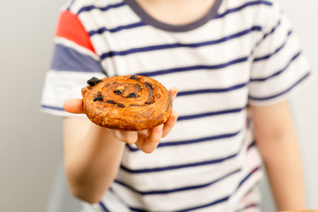 Little joy in hands: A boy holding a sweet raisin bun, a treat-sized happinessの写真素材