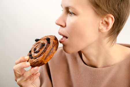 Flavorful enjoyment: A woman of allure delights in a raisin roll, enjoying the flavorful enjoyment of her delightful dessertの写真素材