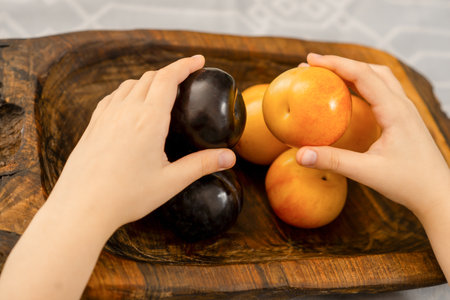 Orchard treasures: Young hands carefully selecting large yellow and blue plums on a wooden platterの写真素材