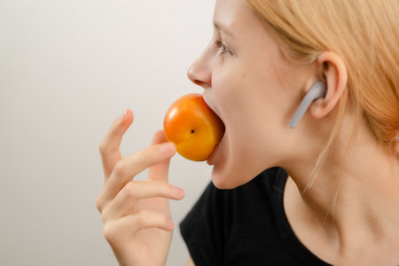 Wholesome teenage treat: A slim young woman enjoys the goodness of a ripe yellow plum, savoring the wholesome delight of her fruity snackの写真素材