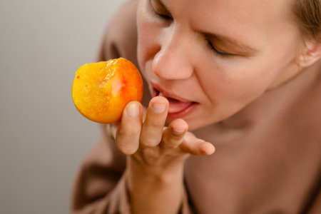 Elegant snacking: A middle-aged lady bites into a juicy yellow plum, elegantly savoring the fruity freshness of her snackの写真素材