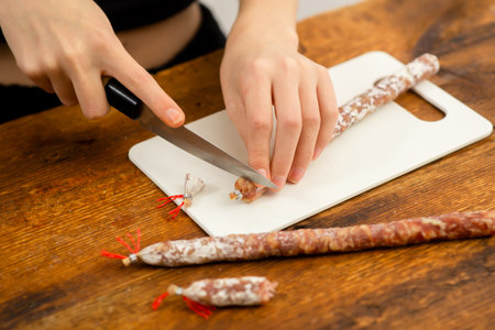 Culinary mastery: Female hands expertly slice sausage on a cutting board, showcasing kitchen skills and the art of food preparationの写真素材