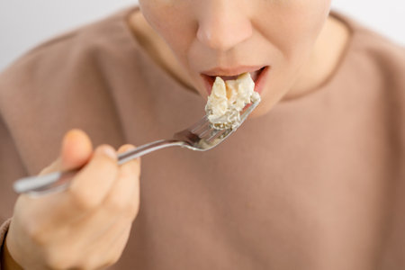 Mayo-infused goodness: A woman indulging in a forkful of a delectable salad, drizzled with creamy mayonnaise and colorful vegetablesの写真素材