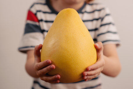 Nutrient-packed delight: a child explores the wonders of a sizable yellow pomelo, promoting the...