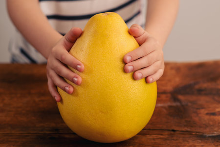 Wholesome nutrition at a glance: a child's hands cradle a generous yellow pomelo, illustrating the nutritional value of this delicious fruit on a wooden settingの写真素材