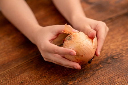 Child's hands cradle a whole onion, celebrating the nutritional benefits of this versatile vegetable on a wooden surfaceの写真素材
