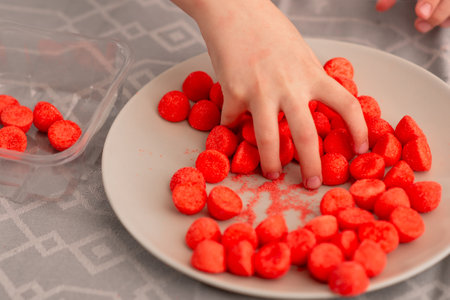 Child's delight: tiny fingers grasp red fruity candies, an adorable portrayal of love for sweets
