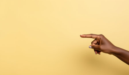 On a cheerful yellow backdrop, a woman's hand points to an unoccupied area, offering a vibrant canvas for your message or creative inputの素材