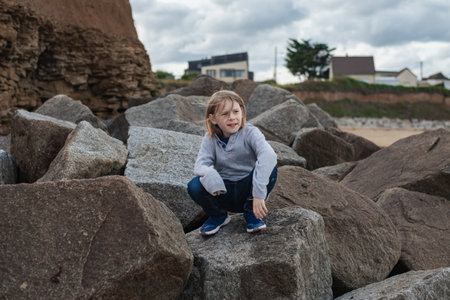A boy with long hair sits contemplatively on large rocksの写真素材