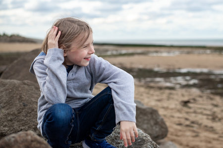 A 10-year-old boy lost in thought while sitting on big rocks