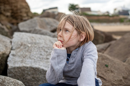 The thoughtful expression of a 10-year-old boy as he sits pensively on the sizable rocksの写真素材