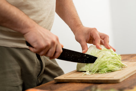 Close-up of hands cutting a head of cabbage on a bamboo cutting board for meal preparation.の写真素材
