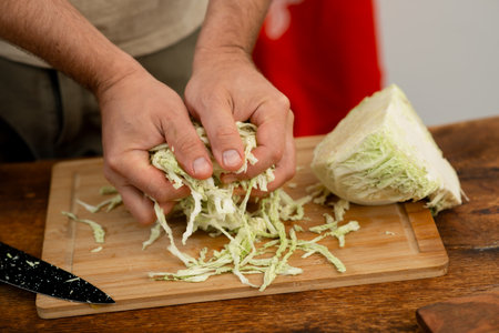 Making fresh coleslaw: hands shredding cabbage on wooden board.の写真素材
