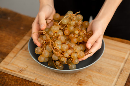 Hands sorting through a cluster of juicy grapes in a gray bowl.の写真素材