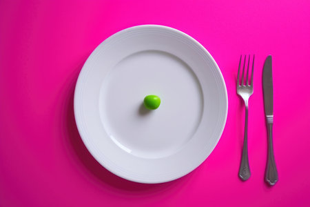 The picture captures a whimsical scene where a lone green pea takes center stage on a pristine white plate, set against a striking pink settingの素材