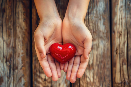Adult hands holding a small red heart gently and compassionately.の素材