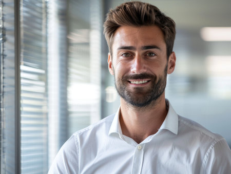 A man with a beard and a smile is standing in front of a window. He is wearing a white shirt and a white tieの素材