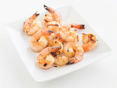 A plate of grilled shrimp with a white background. The shrimp are cooked and seasoned, and they are arranged in a neat row on the plate. Concept of freshness and simplicityの素材