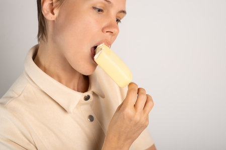 A lady with a trendy pixie cut indulges in ice cream, savoring the sweetness on a pure white...