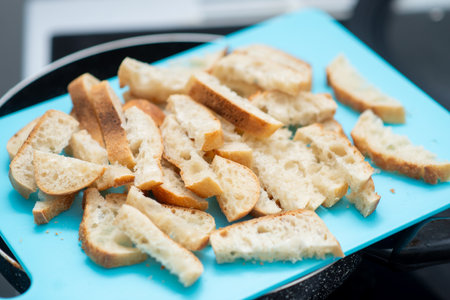 A blue cutting board with bread slices on it. The bread slices are cut into small pieces. Concept of preparation for a meal, as the bread is being cut into smaller pieces to be used in cookingの写真素材