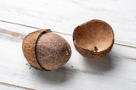 Two coconuts are on a white table. One is whole and the other is cut openの写真素材