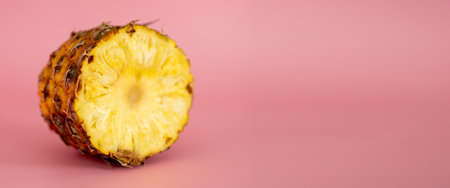 A slice of pineapple is shown on a pink background. The slice is cut in half, revealing the juicy, yellow fruit inside. Concept of freshness and natural beautyの写真素材