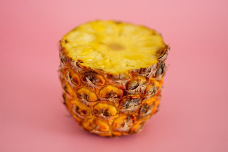A slice of pineapple is cut in half and placed on a pink background. Concept of freshness and natural beauty, as the vibrant yellow color of the pineapple contrasts with the pink backgroundの写真素材