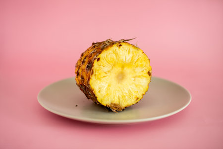 A slice of pineapple is cut in half and placed on a white plate. The image has a bright and cheerful mood, as the pineapple is a symbol of tropical fruits and vacationsの写真素材
