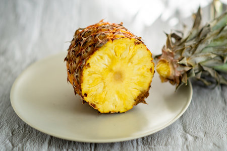 A slice of pineapple is cut in half and placed on a white plate. Concept of freshness and natural beauty, as the vibrant yellow fruit is displayed in its natural stateの写真素材